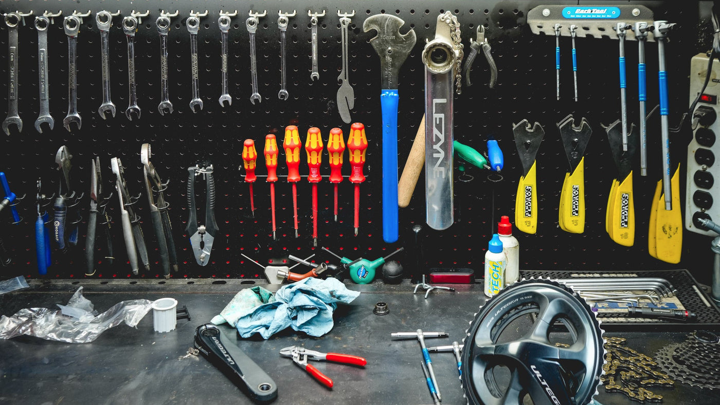 Workbench with tools and equipment, including a wheel and various tools on a black pegboard background.