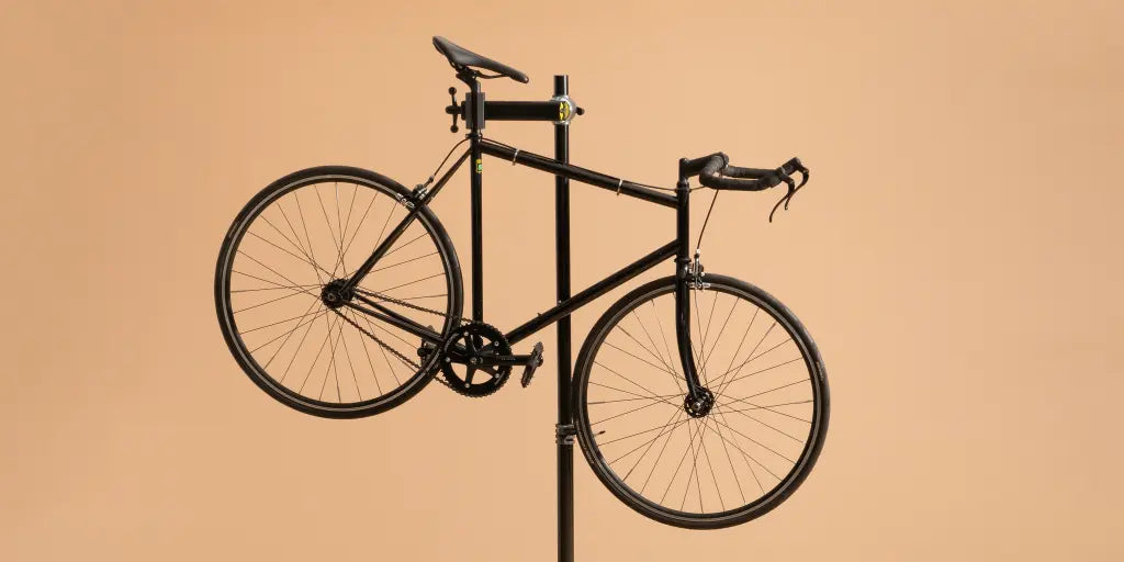 A black road bicycle displayed on a black vertical stand against a solid warm beige background.